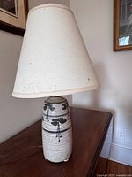 Photo of ceramic table lamp with beige fabric shade on wooden surface against cream wall.