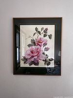 Framed watercolor painting showing two large pink roses and rosebuds with green leaves in a dark green mat and wood/gold trim frame.