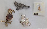 All four brooches and pins displayed together on white background with owl, bird, cat pair, and small figure pin