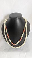 Front view of double-strand beaded necklace displayed on a black bust, showing shell, coral, and glass bead details.