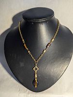 Full view of the gold-tone chain necklace displayed on a black jewelry stand showing amber and brown glass beads with a geometric pendant.