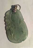 Front view of the light green jade pendant showing carved floral vine design and metal bail with flower decoration.
