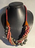 Front view of chunky multi-strand wooden bead necklace displayed on a black mannequin bust. Shows natural, red, and dark grey wooden beads twisted together with cone-shaped wood caps.