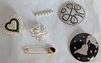Top view of 6 costume jewelry brooches and pins on white background