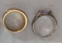 Top view of two rings: one gold-plated with decorative stones, one silver-tone with a light purple stone.