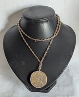 Full view of the gold-tone twisted rope chain necklace with a vintage coin pendant displayed on a black mannequin bust.