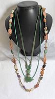 Front view of the multi-strand necklace displayed on black bust. Shows green, orange, turquoise, purple, and gold toned beads with green stone bear pendant.