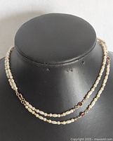 Front view of a double-strand pearl and gold-tone princess necklace with red glass gemstone accents, displayed on a black jewelry bust.