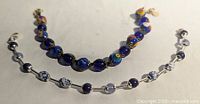 Close-up view of the two bracelets highlighting the blue, multi-color, and white glass beads with Millefiori and Murano style patterns along with lobster clasp closures.