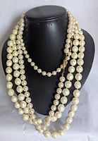 Three ivory-colored imitation pearl necklaces displayed on a black bust. Necklaces vary in length and bead size, including a choker style.