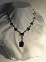 Full view of silver tone necklace displayed on a white fabric bust showing the black rectangular faceted stones and pendant.