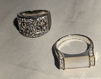 Photo showing two costume jewelry rings: one with a rectangular cluster of clear rhinestones and the other with a rectangular mother of pearl inlay bordered by rhinestones