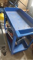 Blue 2-tier metal garage trolley showing top and bottom tray with some dirt and wear.
