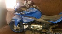 Side view of blue electric ride-on motorcycle seat, front, and part of the control panel.