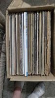 Top-down view of approximately 40 vinyl LP records tightly packed in a cardboard box, showing worn edges and aged spines.