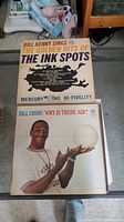 Vinyl record albums featuring Bill Kenny Sings The Golden Hits of The Ink Spots and Bill Cosby Why Is There Air? visible on top of stack.
