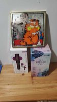 Garfield clock displayed atop boxes of portable garment steamer and boxed wine glass on a wooden surface