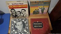 Four vinyl LP albums on a table including The Mills Brothers albums, a Philharmonic classical album, and Remember Glenn jazz album, showing front covers and artwork.