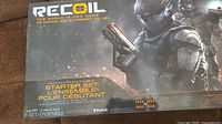 Front of the Recoil The World is Now Game starter set box showing branding, age rating, multiplayer support up to 16 players, and Bluetooth compatibility.