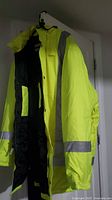 Front and side view of yellow high-vis winter coat with attached hood showing reflective stripes and black quilted interior lining.