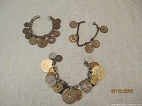 Three coin charm bracelets displayed on cloth
