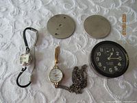 Group shot of all items: wristwatch, pendant watch with chain, car clock, two metal plates