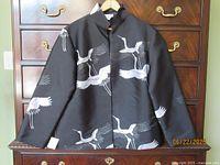 Front view of black jacket with crane print displayed on dresser