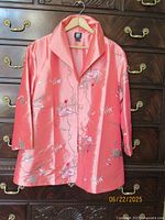 Front view of coral pink embroidered jacket on hanger