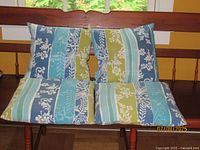 Front view of four blue, green and white floral stripe patio cushions placed on bench