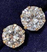 Close-up photo showing one 10K gold earring with round clear cubic zirconia stone in six-prong setting on dark background