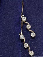 Pair of 10K gold earrings with hook backs and three clear round cubic zirconia stones arranged vertically on a wavy gold setting.