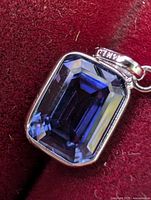 Front view of emerald-cut tanzanite pendant on red velvet background
