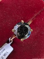 Front view of ring on red velvet background showing round black diamond in four-claw setting