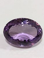 Close-up of oval, faceted genuine amethyst gemstone showing light to medium purple color and faceted cut on crown surface.