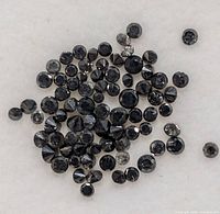 Multiple round-cut black onyx faceted gemstones spread out showing varying sizes and reflective facets on a light background.