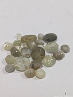 Multiple cat's eye cabochon gemstones arranged on white surface showing color variation and distinctive cat's eye effect.