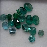 Close-up photo of 16 loose genuine emerald gemstones showing various shapes and faceting.
