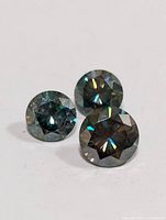 Three round faceted genuine moissanite gemstones photographed on a white background showing the cut and color characteristics.