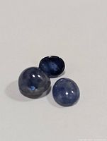 Three polished sapphires arranged in a triangular grouping on a plain white background showing color and surface texture.