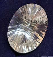 Close-up of the oval cut white topaz showing detailed faceting and transparency on dark background.