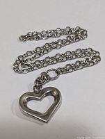 Sterling silver necklace with open heart pendant laid out on white background, showing chain and clasp details.