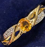 Close-up of silver ring with orange-yellow round cut gemstone and clear stone accents on band