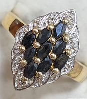 Close-up top view of silver ring with dark blue marquise-cut sapphire stones surrounded by clear accent stones, displaying the cluster design on top.