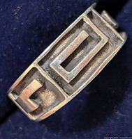 Close-up of silver ring showing geometric raised rectangular and square design on band.