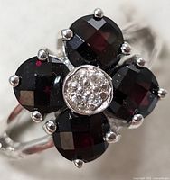 Close-up of silver ring with four garnet stones and central clear stones cluster.