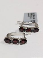 Side angle of both silver garnet earrings with a label detailing silver weight and garnet carat weight.
