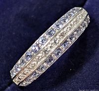 Close-up photo of sterling silver ring showing two rows of round cut tanzanite stones and central textured metal band.