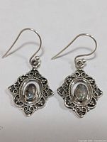 Pair of silver earrings with ornamental design featuring oval labradorite stones, front view.