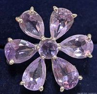 Close-up photo of the ring showing six pear-shaped amethyst stones arranged as flower petals with one round amethyst center stone in sterling silver prong settings on a dark cloth background.