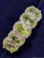 Close-up photo showing five oval cut peridot stones in sterling silver setting with twisted rope detail around each stone.